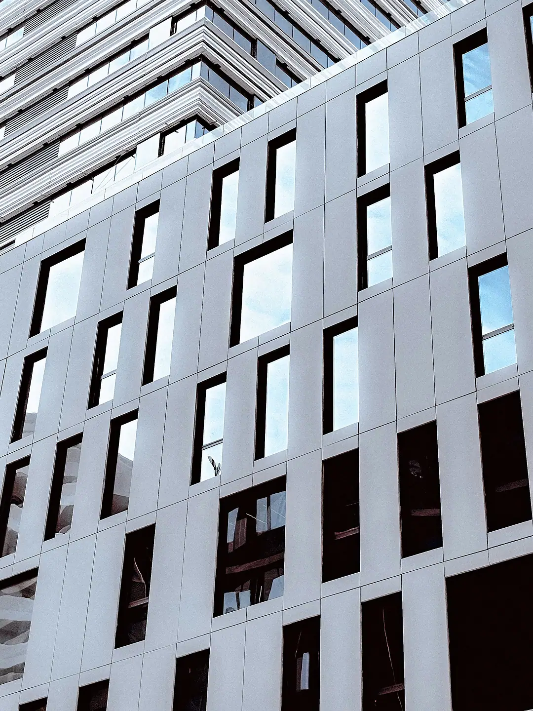 The facade of an office tower in Casablanca: white panels and staggered deep-set windows reflecting the sky