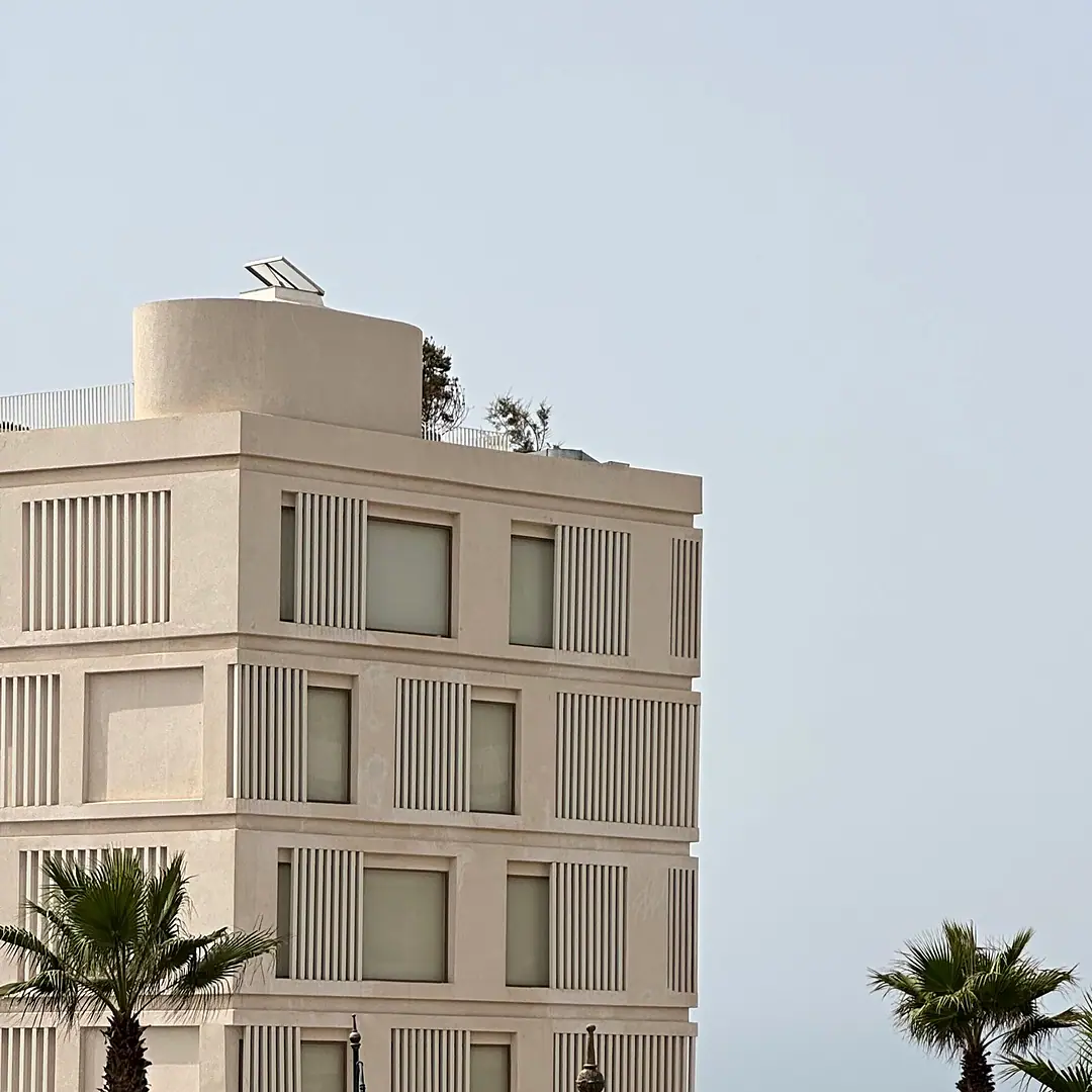 A new stone building with deep window reveals on the Moroccan Atlantic coast, palms and the ocean beside it