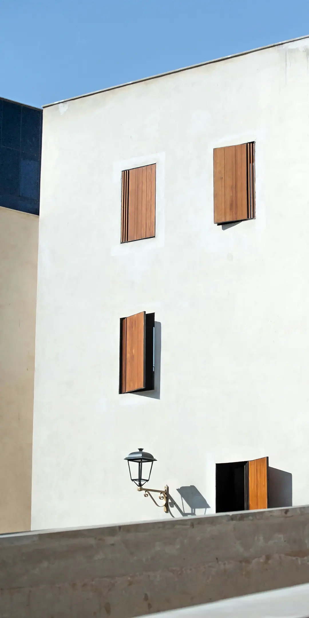 A white rendered building in Fez with timber shutters, beside a wall of red geometric tiles