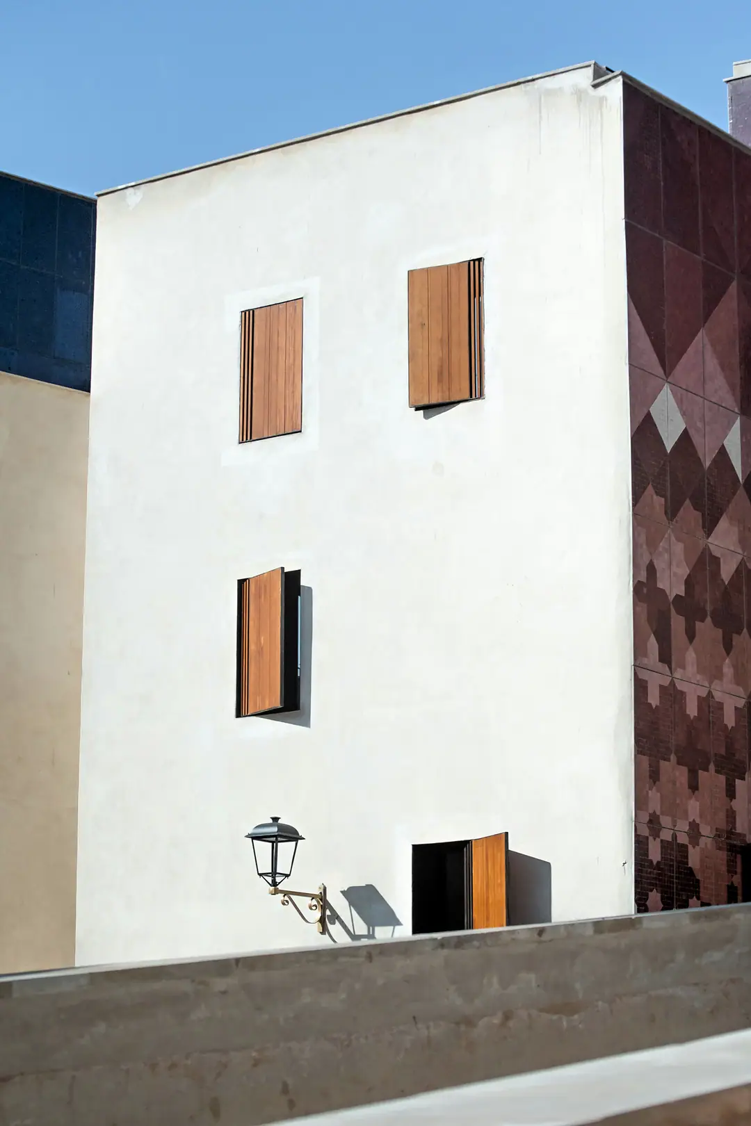 A white rendered building in Fez with timber shutters, beside a wall of red geometric tiles