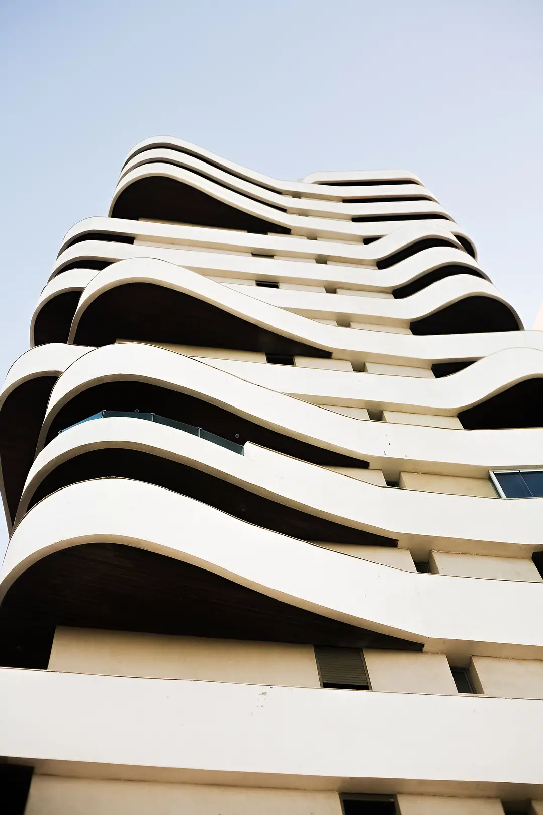 White curving balcony bands of a contemporary building rising into a pale sky