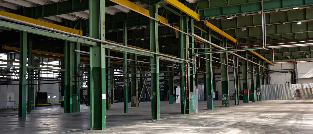 An empty factory hall with green steel columns, yellow crane rails and a concrete floor