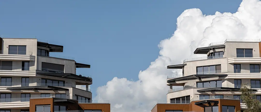 Terraced white apartment buildings with timber screens under a blue sky and a towering cloud