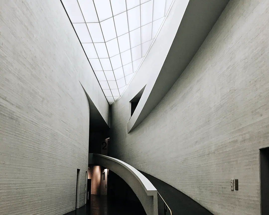 A daylit museum hall: curved white walls under a long skylight, a ramp sweeping down to the floor below