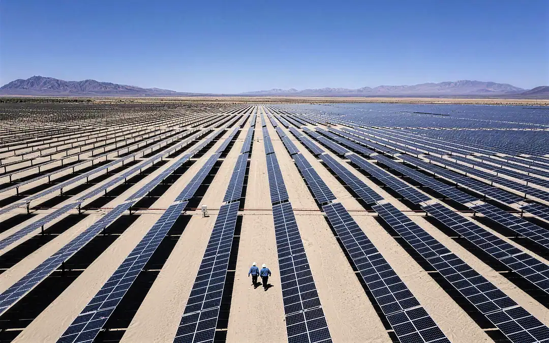 A large photovoltaic plant from the air, two technicians in hard hats walking between the rows of panels