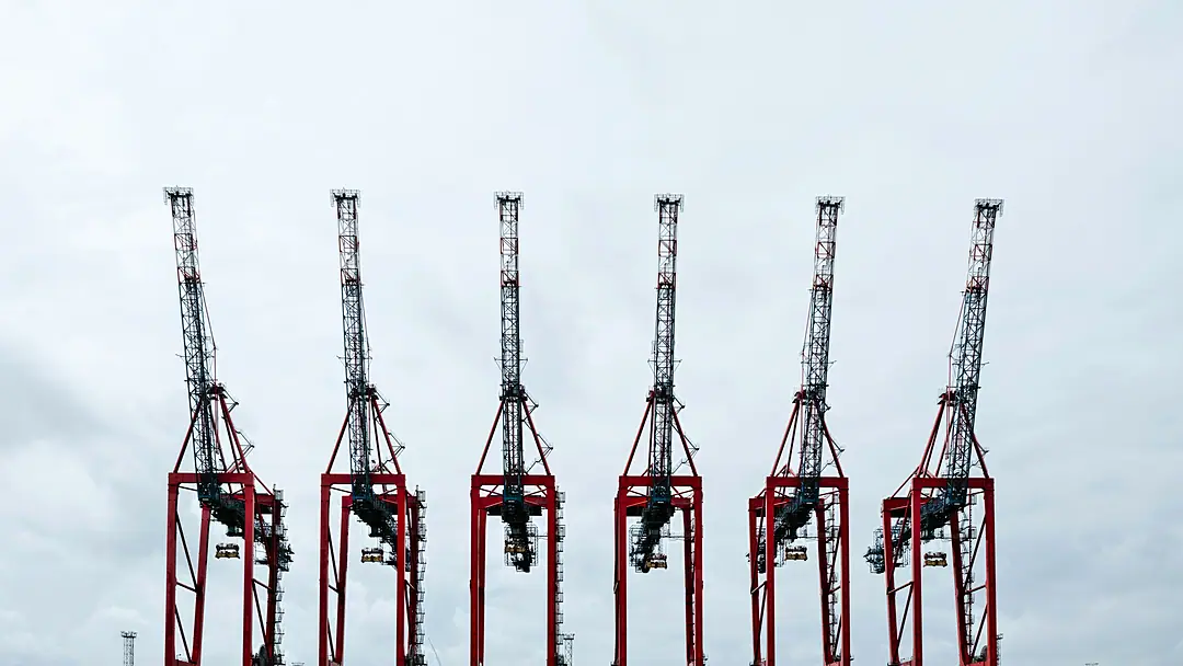 A row of six ship-to-shore cranes against an overcast sky