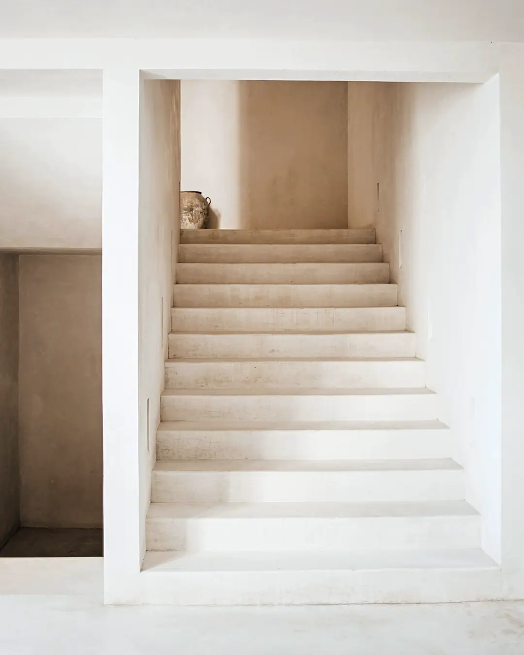 A plastered stair rising through a white opening in soft daylight
