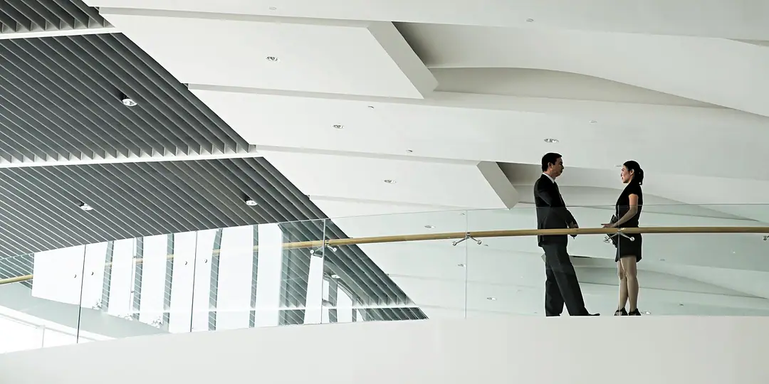 Two people in conversation on a white curved gallery in a bright contemporary atrium