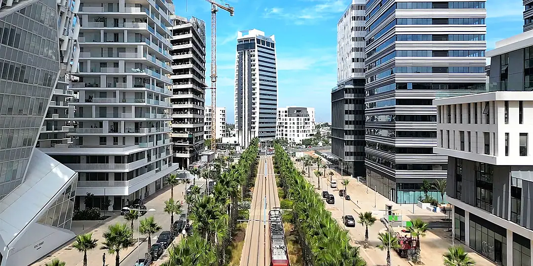 A wide boulevard lined with palms and new office towers, a tram line down its centre and a tower crane on the skyline
