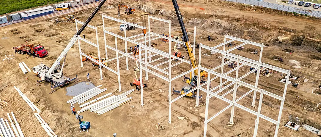 Aerial view of a steel building frame going up on a cleared industrial plot, a mobile crane at work