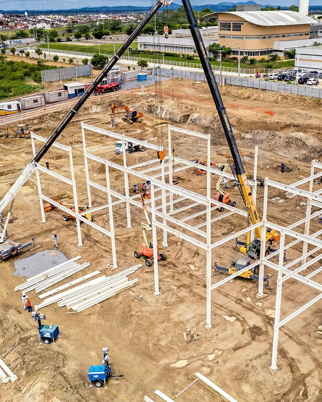 Aerial view of a steel building frame going up on a cleared industrial plot, a mobile crane at work